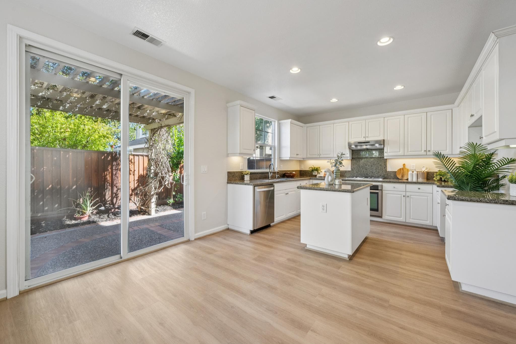 Wide kitchen with white cabinetry, center island, recessed lights, and a sliding door to the patio